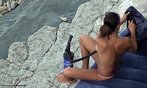 Amateur en culotte violette surprise topless sur plage cachée. Sait-elle qu'un voyeur la regarde bouger nue ?