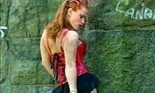 Latex-Clad Redheaded Mistress Poses Seductively by the Wall.