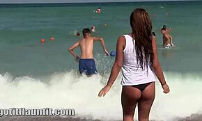 Cheerful college chick lifts her top on a crowded public beach